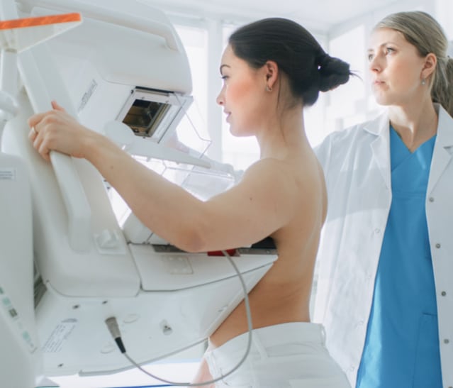 woman undergoing exam standing in mammogram machine