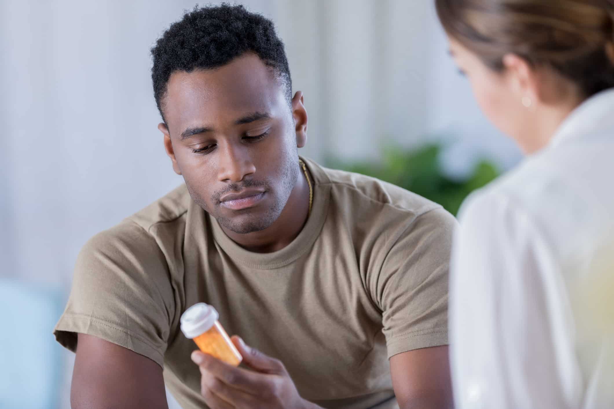 A female doctor perscribing an African American man pain medication. He's hold the pain medication and reading the label.