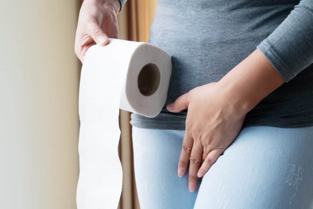 Disorder, Diarrhea, incontinence. Healthcare concept. Woman hand holding her crotch lower abdomen and tissue or toilet paper roll.