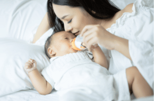 little boy drinking a milk from bottle in the mom's arms and kissing her baby