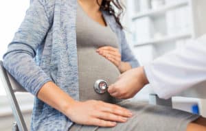 gynecologist doctor with stethoscope listening to pregnant woman baby heartbeat at hospital 300x191 1