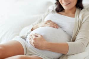 happy smiling pregnant woman lying in bed and touching her belly